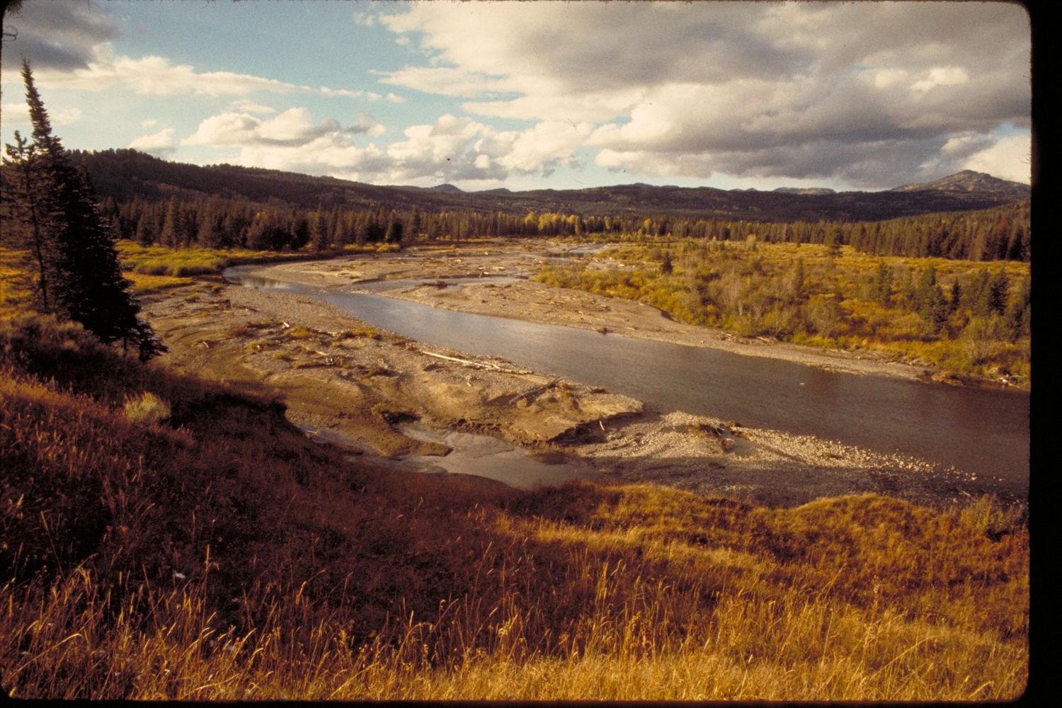 A river winding through autumn bottomland below the forest, the range on the skyline.